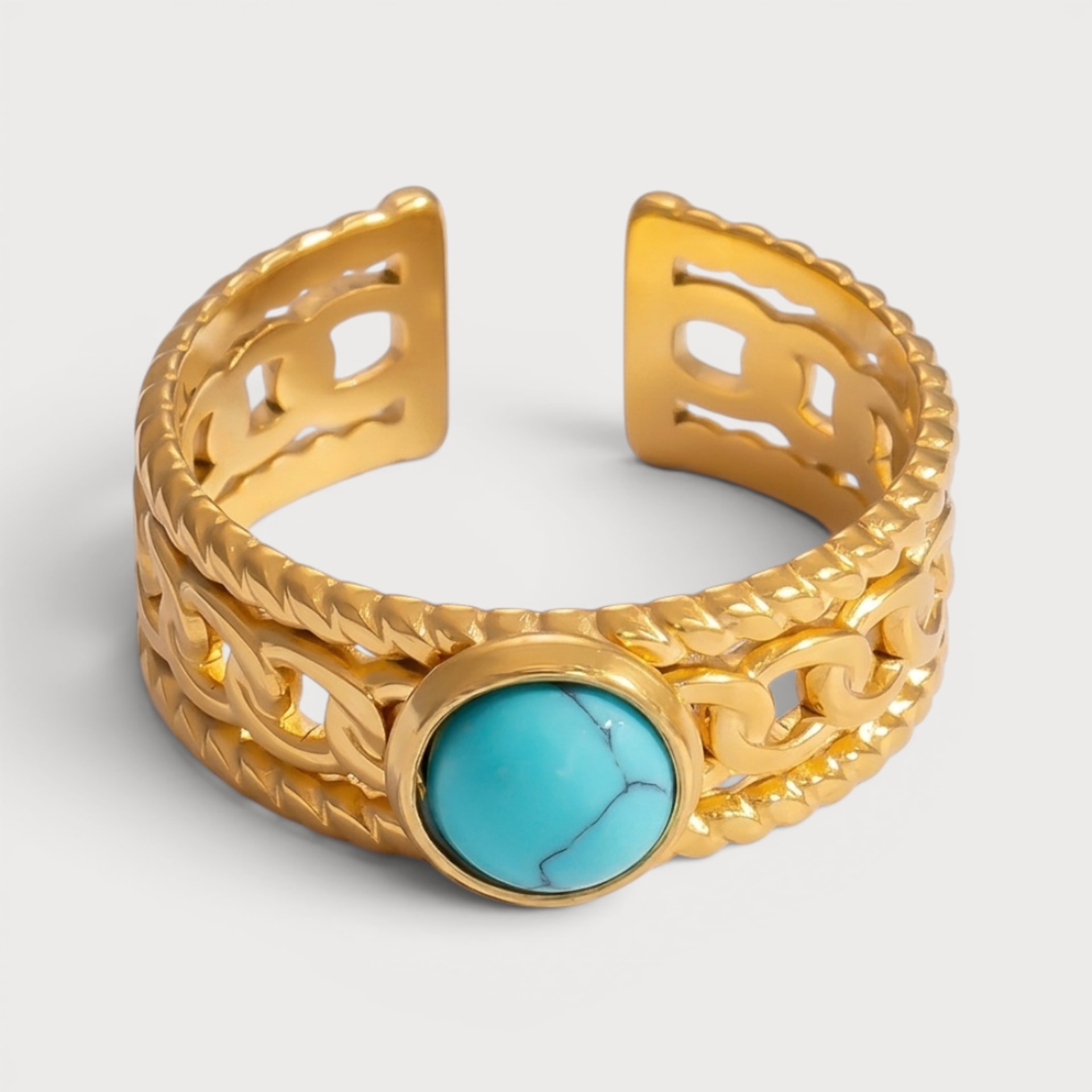 Bague Éveline : une pierre ronde turquoise se détache sur une large bande dorée à motifs géométriques ajourés.