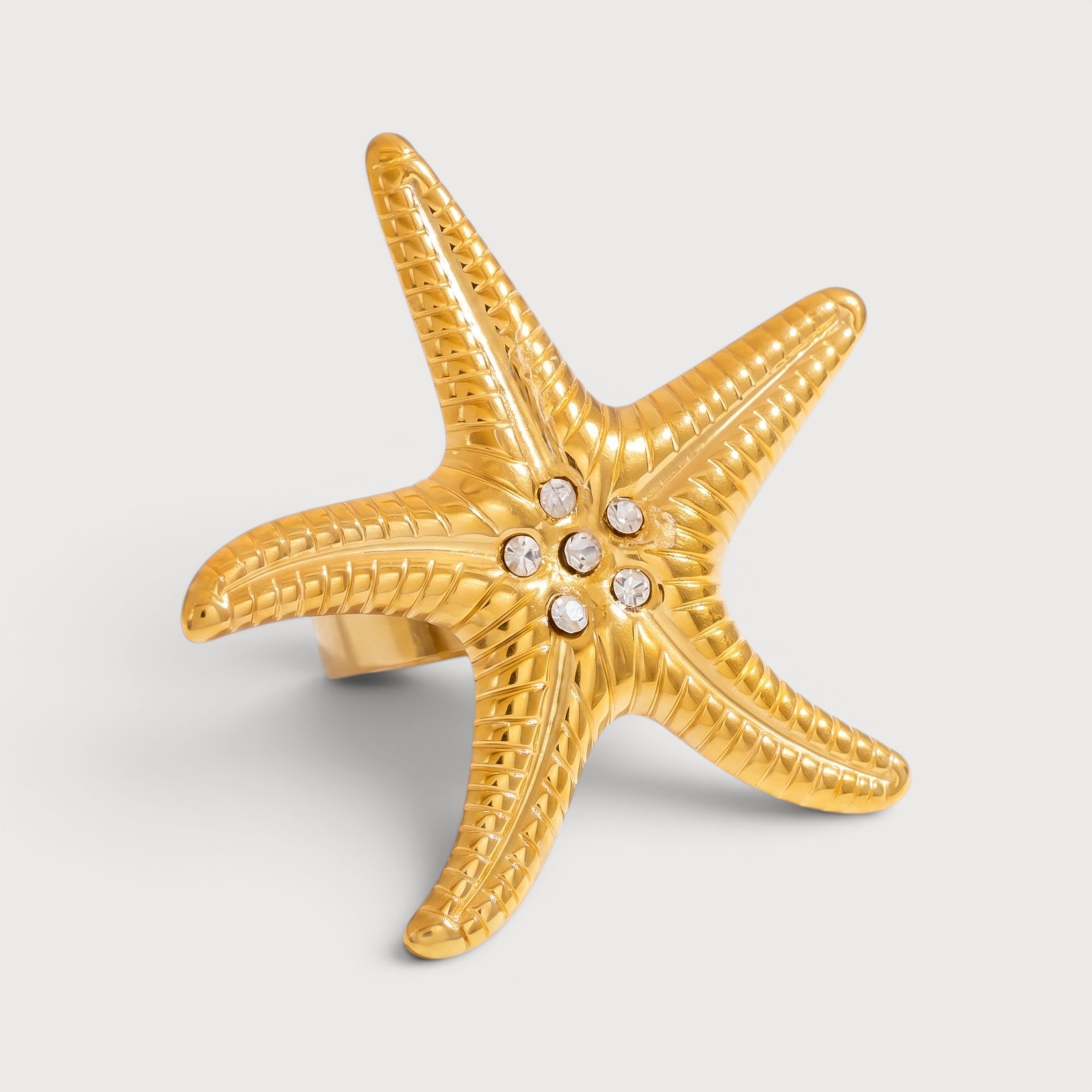 Bague Hortense : une étoile de mer dorée porte un groupe de pierres claires au centre.
