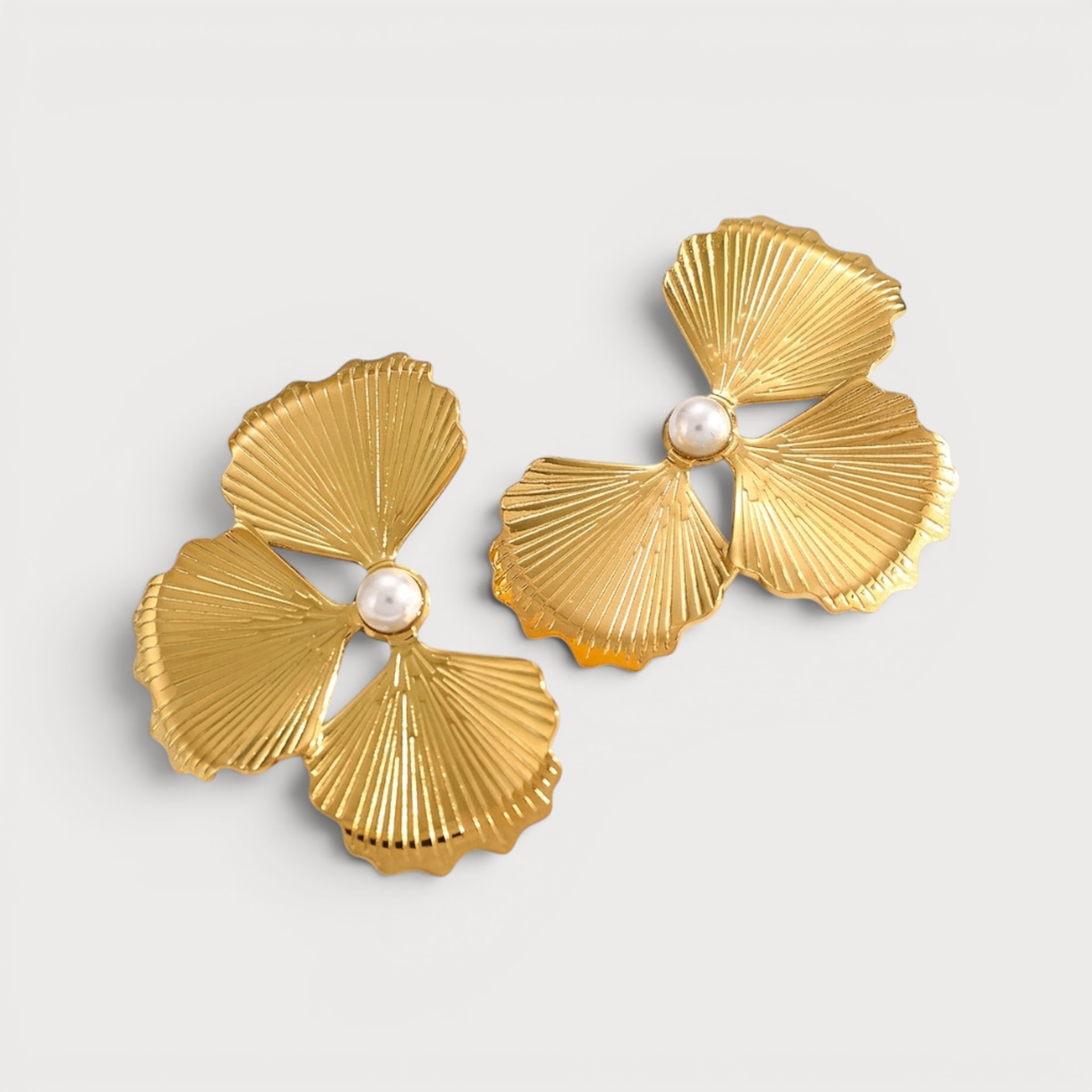 Boucles d’oreilles Cheïma : trois pétales en éventail dorés se rejoignent autour d’une perle blanche.
