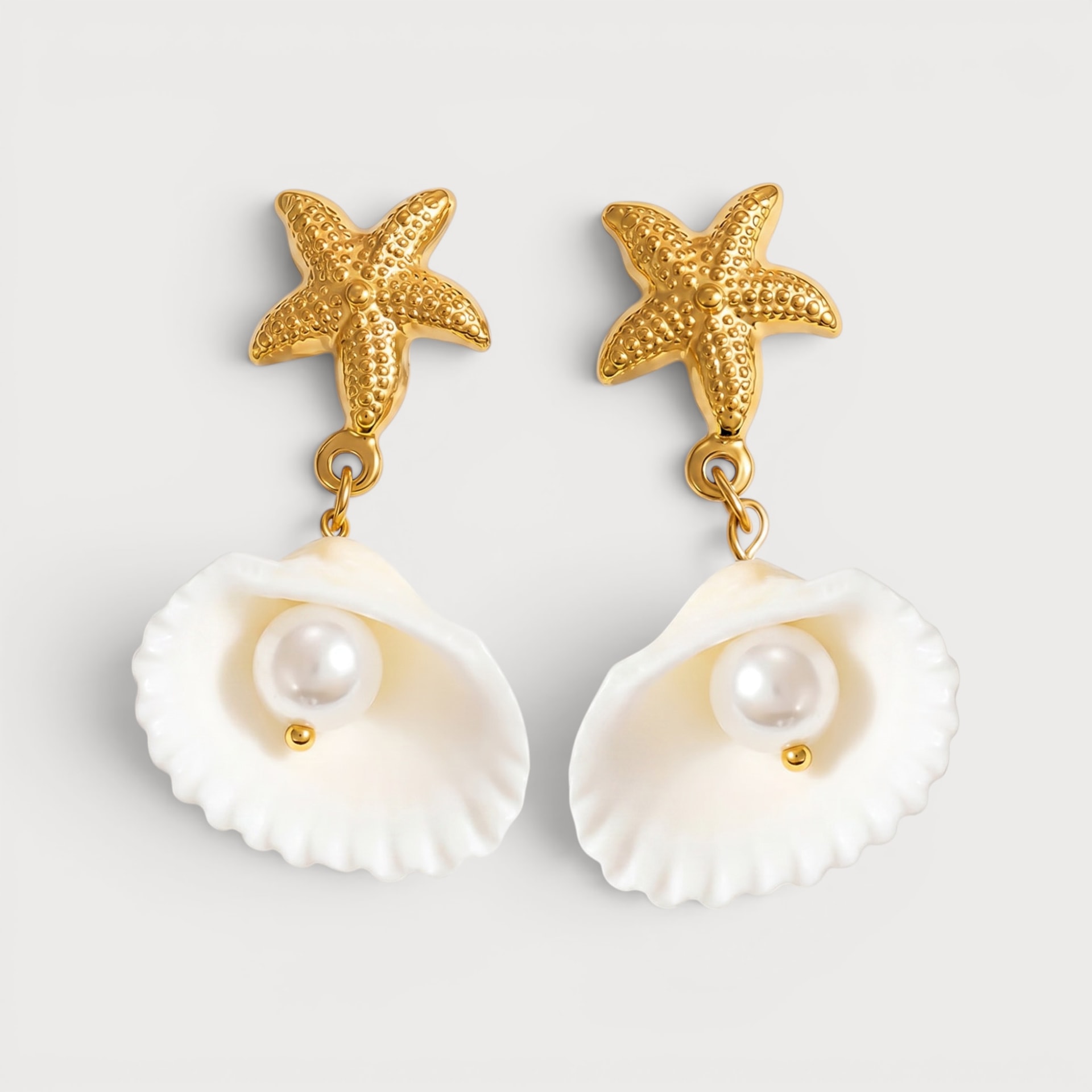 Boucles d’oreilles Vittoria : une étoile de mer dorée retient un coquillage blanc arrondi avec une perle au centre.