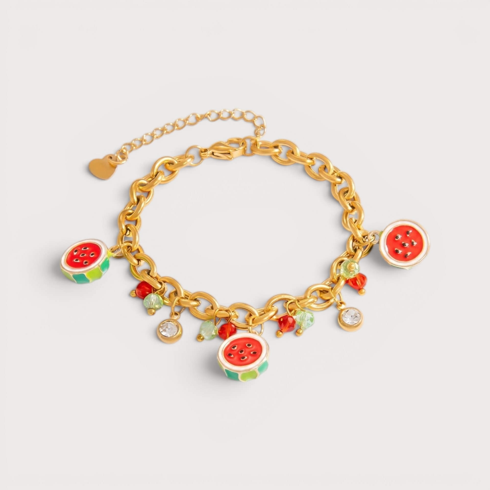 Bracelet Aurora : des breloques pastèque rouges et vertes ponctuent une chaîne dorée avec de petits détails clairs.
