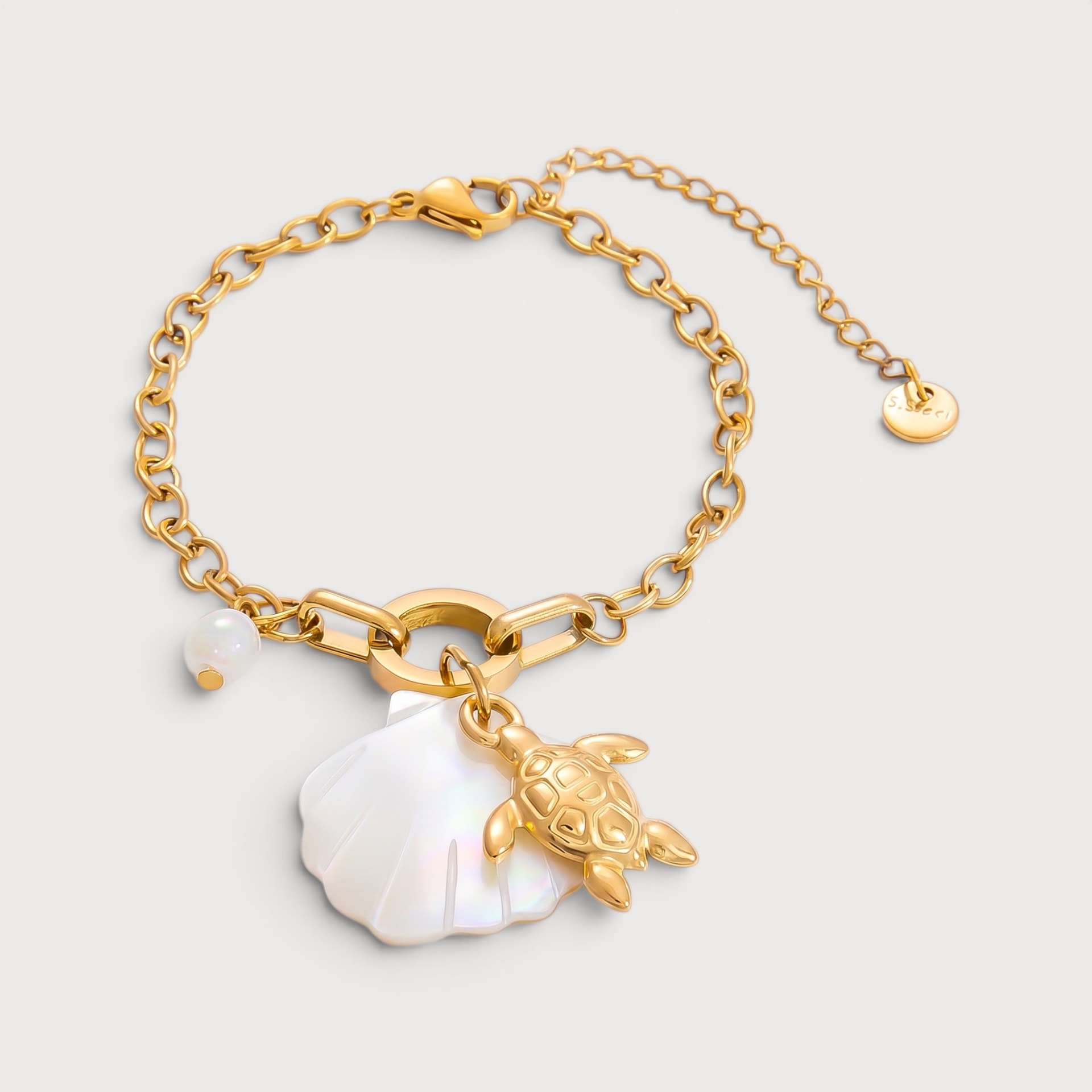 Bracelet Cleïa : un grand coquillage blanc irisé et une tortue dorée pendent au centre d’une chaîne à maillons.