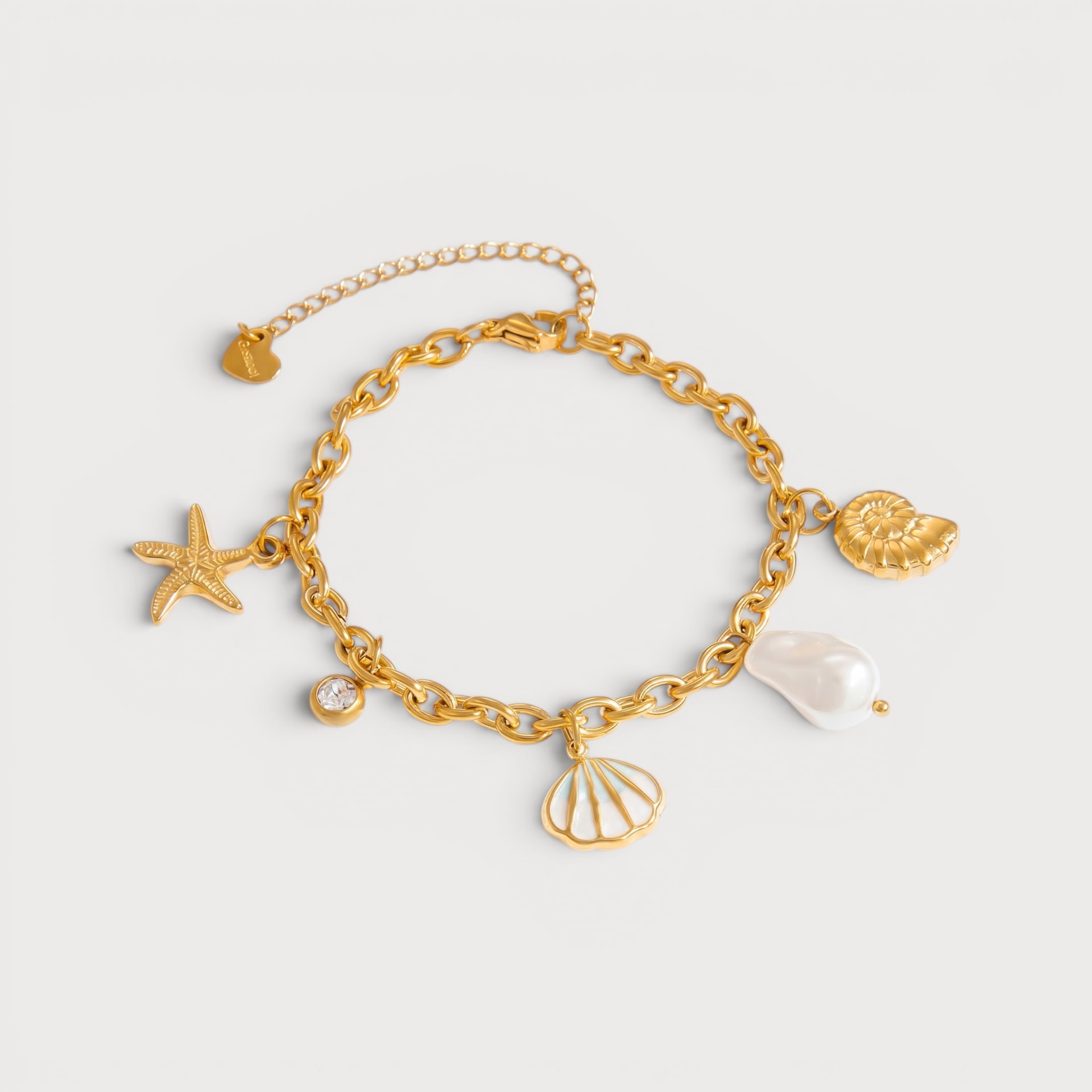 Bracelet Gloria : une chaîne dorée porte une étoile de mer, un coquillage ajouré, une coquille spiralée et un détail blanc irrégulier.
