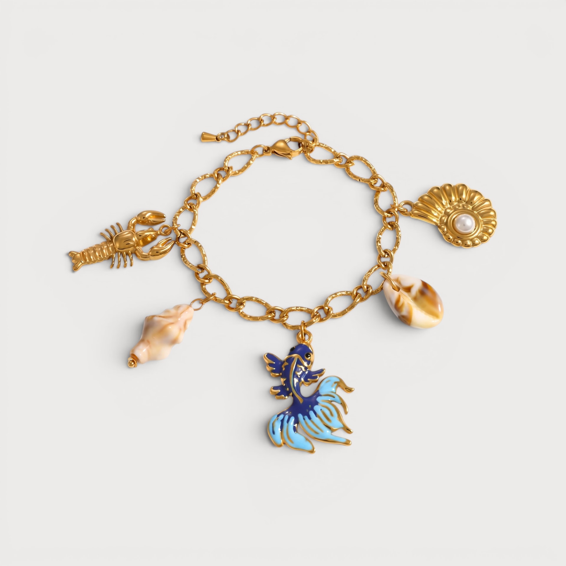 Bracelet Phoébé : une chaîne à maillons dorés porte un poisson bleu, un homard, un coquillage spiralé et d’autres petites breloques marines.