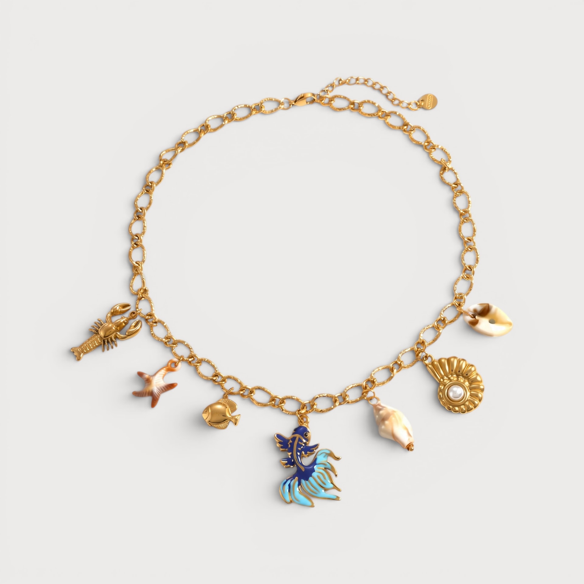 Collier Hyacinthe : une chaîne à maillons dorés porte des motifs coquillage et une petite breloque poisson colorée au centre.