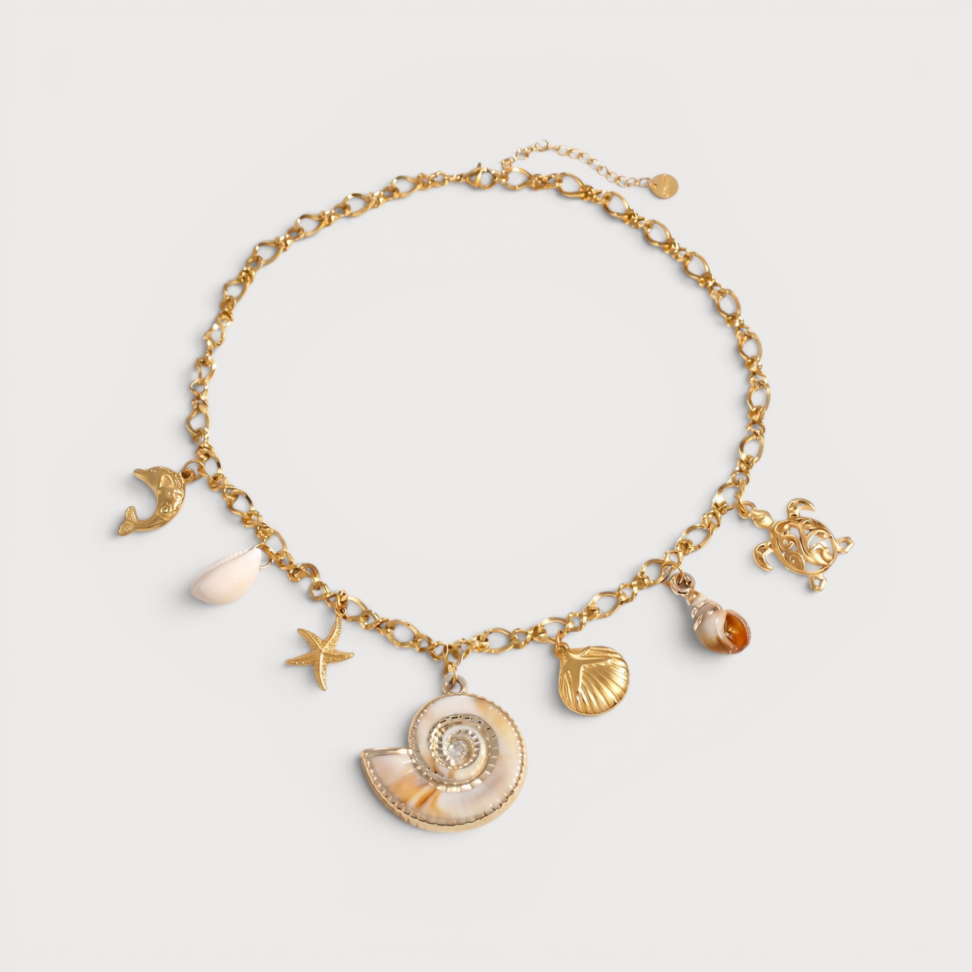Collier Marília : une chaîne à maillons dorés porte un grand coquillage spiralé, une étoile de mer et plusieurs petites breloques marines.