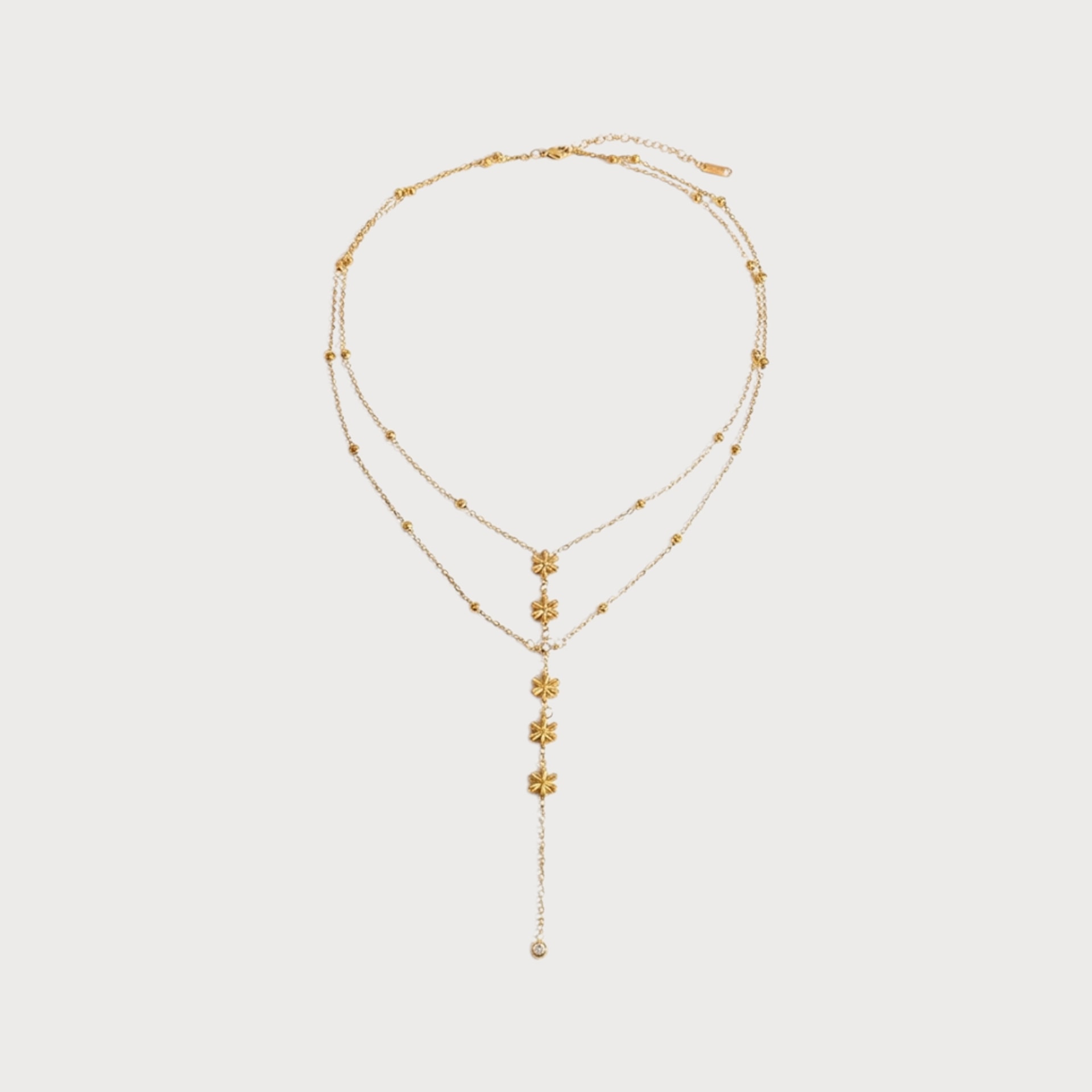 Collier Prudence : deux chaînes dorées superposées, ponctuées de petites billes, se prolongent par une chute ornée de fleurs.