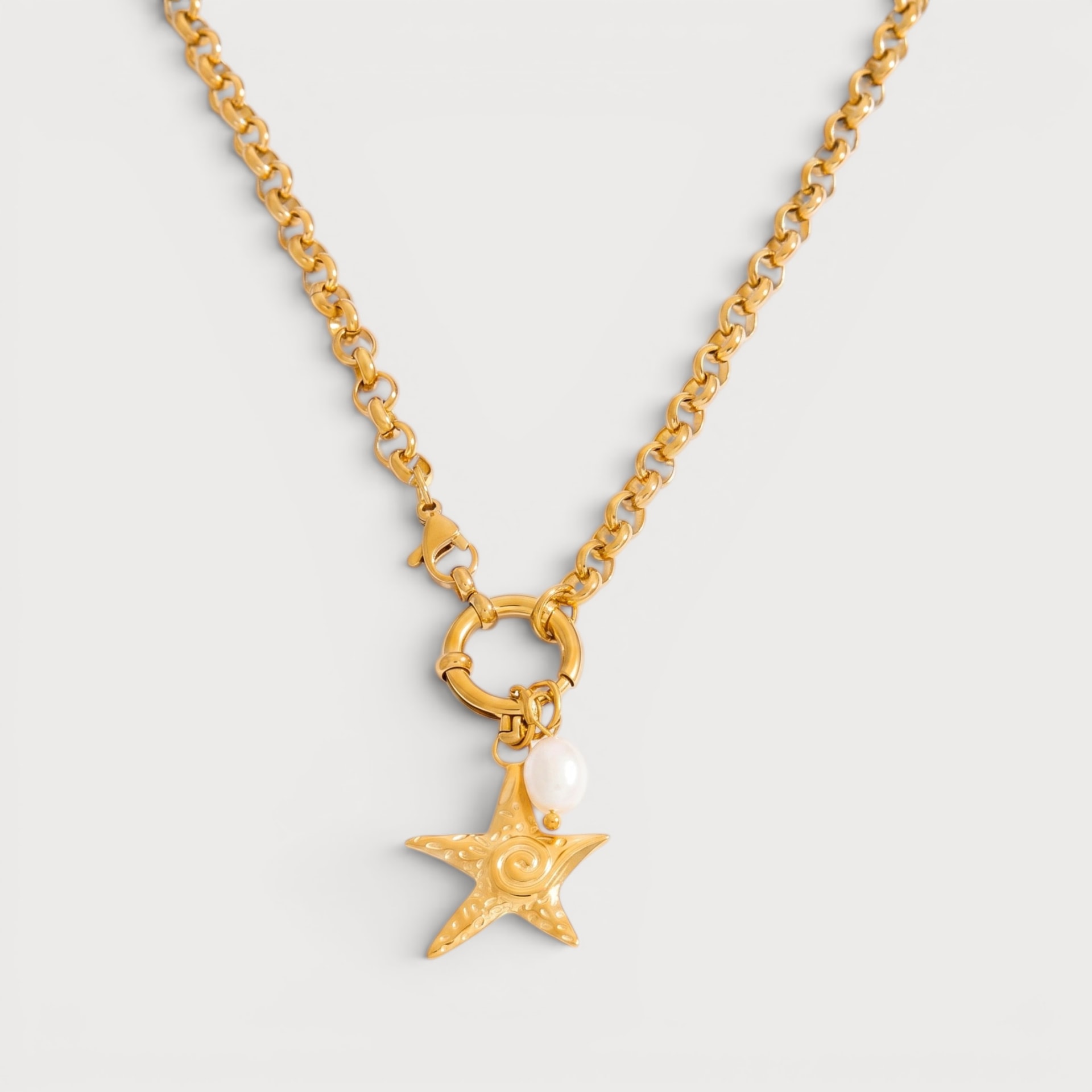 Collier Yana : une chaîne dorée à maillons rejoint un fermoir rond portant une étoile de mer et un détail blanc irrégulier.
